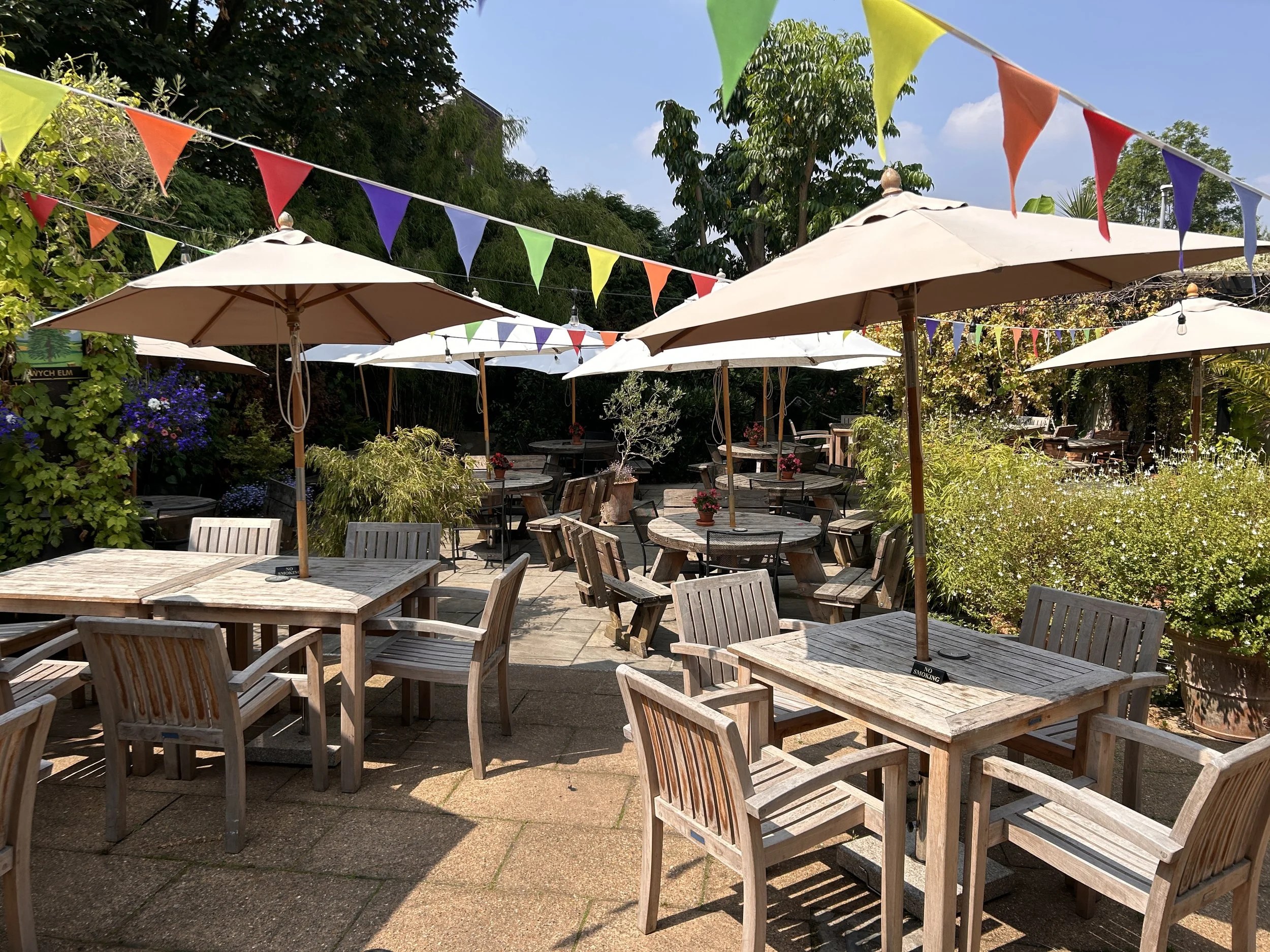 The leafy pub garden with wooden tables, parasols and bunting